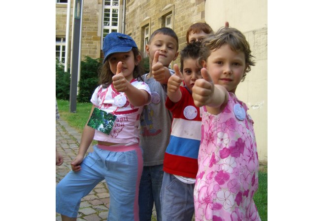 F&uuml;nf Kinder stehen in einer Reihe und zeigen den Daumen nach oben. Sie befinden sich vor einem alten Geb&auml;ude mit Backsteinmauern., &copy; Touristik und Marketing GmbH