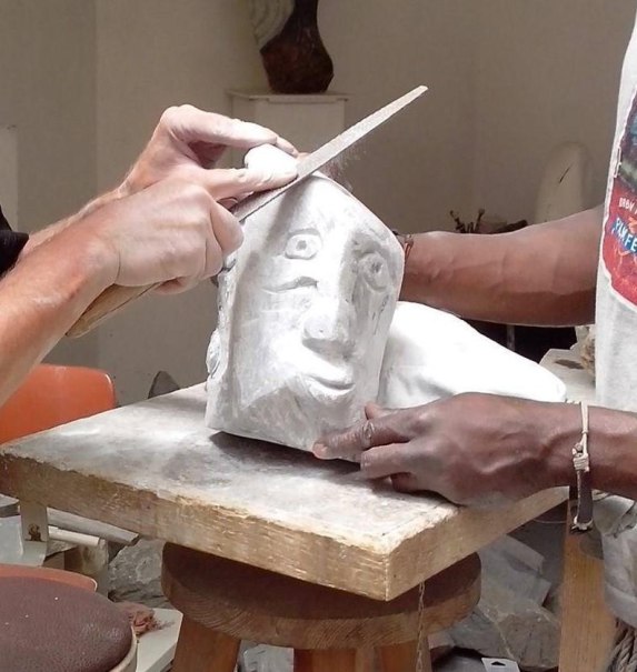 Zwei Personen bearbeiten eine Steinskulptur mit einem Gesicht. Eine Person feilt, während die andere die Skulptur hält. Der Workshop findet in Ludwigsburg statt., © Kunstschule Labyrinth