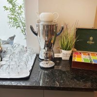 Teestation mit Gl&auml;sern, Teebeuteln und einem Wasserkocher auf einer schwarzen Theke. Dekorative Pflanze und Teebox vorhanden., &copy; Novum Hospitality