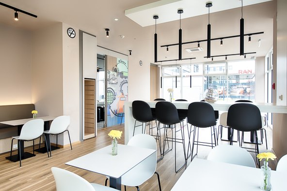 Moderner Frühstücksbereich mit weißen Tischen, schwarzen Stühlen und gelben Blumen in Vasen. Große Fenster lassen viel Licht herein., © B&B Hotel Stuttgart-Neckarhafen