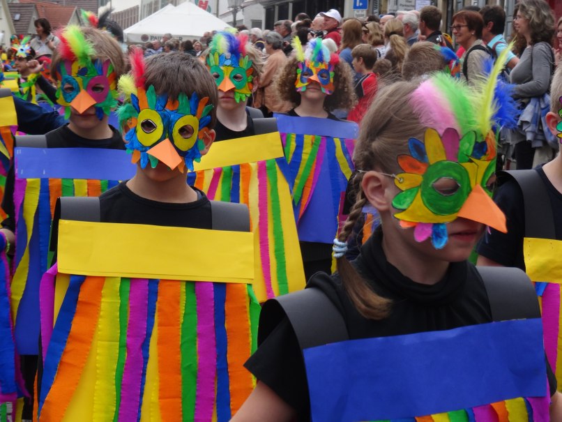 Kinder tragen bunte Vogelmasken und Kostüme beim Maientag in Nürtingen. Sie sind Teil eines fröhlichen Umzugs mit vielen Zuschauern., © Stadt Nürtingen