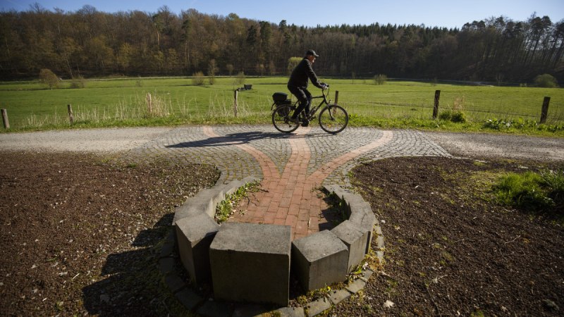 Ein Radfahrer f&auml;hrt auf einem gepflasterten Weg durch eine gr&uuml;ne Landschaft mit Wiesen und W&auml;ldern im Hintergrund., &copy; VRS/ Stoppel