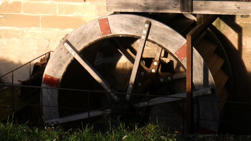 Ein altes h&ouml;lzernes M&uuml;hlrad mit Metallverst&auml;rkungen, das an einer Steinmauer befestigt ist. Sonnenlicht f&auml;llt auf das Rad., &copy; Stadtmarketing Leonberg
