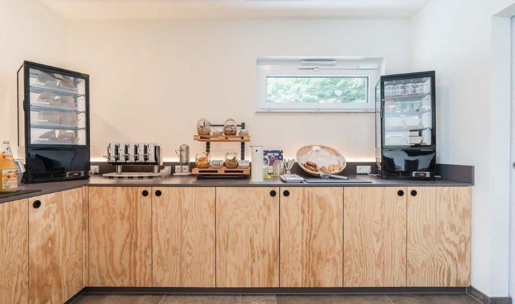 Ein Fr&uuml;hst&uuml;cksbuffet mit Brotk&ouml;rben, Kaffeemaschine und Getr&auml;nken auf einer Holztheke in einem hellen Raum., &copy; a2 HOTELS am Quadrium
