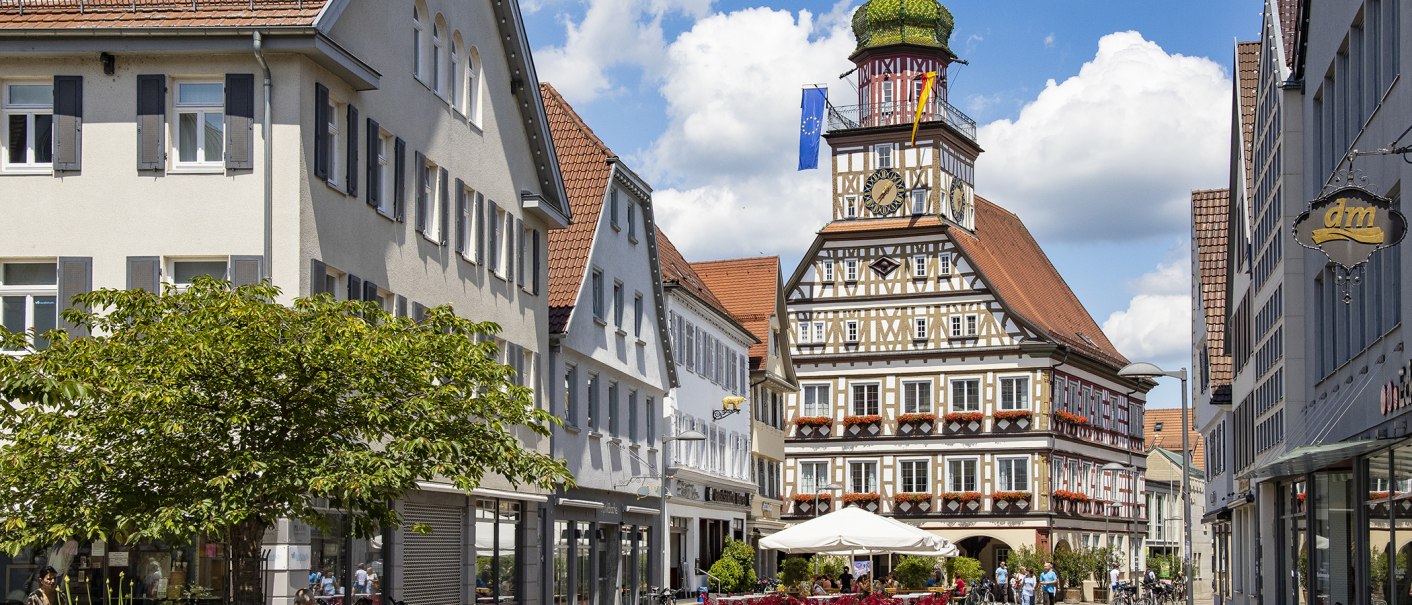 Das Fachwerk-Rathaus von Kirchheim unter Teck mit Uhrturm, umgeben von historischen Gebäuden und einem belebten Platz mit Cafés., © Torsten Wenzler