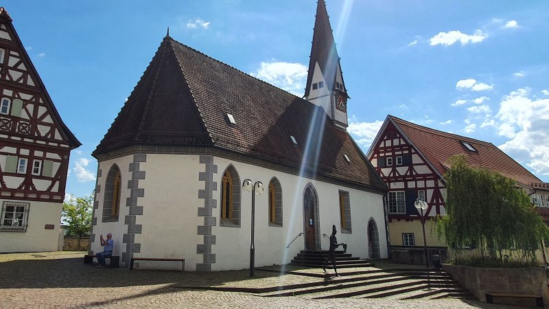 Die Ottilienkapelle mit spitzem Turm und Fachwerkhäusern im Hintergrund, bei sonnigem Wetter und blauem Himmel., © PlochingenInfo Die Ottilienkapelle mit spitzem Turm und Fachwerkhäusern im Hintergrund, bei sonnigem Wetter und blauem Himmel., © PlochingenInfo