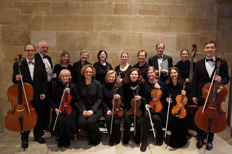 Ein Kammerorchester posiert vor einer Steinwand. Die Musiker halten Streich- und Blasinstrumente und tragen formelle Kleidung., © Schönblick gemeinnützige GmbH