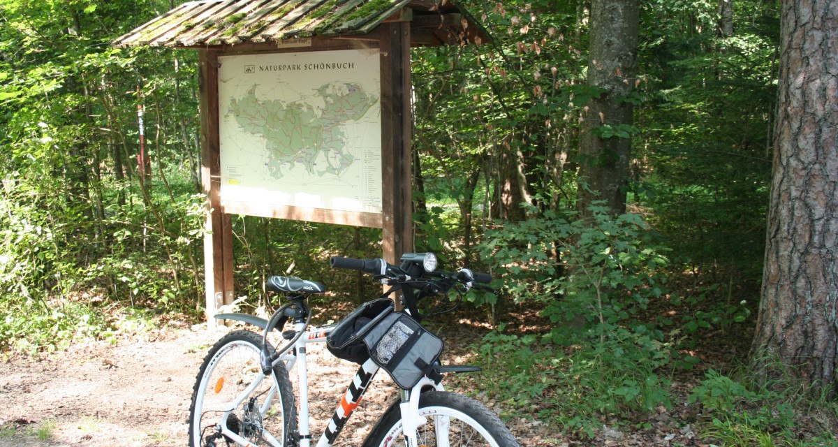 Ein Fahrrad steht vor einer Informationstafel im Naturpark Sch&ouml;nbuch. Der Wald im Hintergrund ist dicht und gr&uuml;n., &copy; Natur.Nah. Sch&ouml;nbuch & Heckeng&auml;u