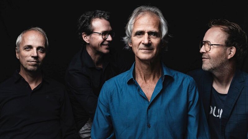 Vier M&auml;nner posieren vor einem dunklen Hintergrund. Der Mann in der Mitte tr&auml;gt ein blaues Hemd, die anderen sind in dunkler Kleidung., &copy; Interessengemeinschaft Kultur Sindelfingen / B&ouml;blingen e.V.