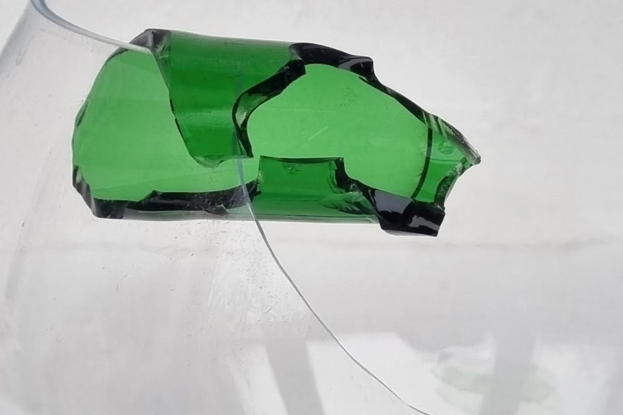 Ein zerbrochenes grünes Glasstück schwebt vor einem weißen Hintergrund. Die Kanten sind unregelmäßig und scharf., © Bettina Funke