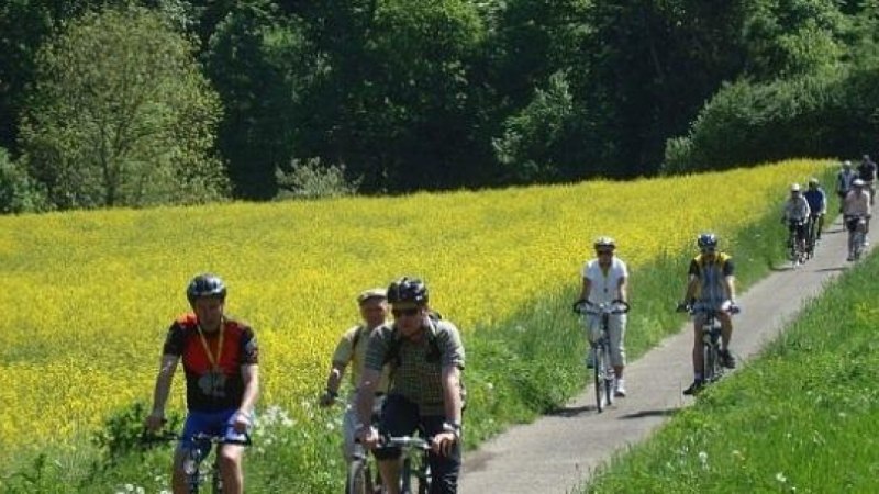 Radfahrer auf einem schmalen Weg neben einem gelben Rapsfeld, umgeben von grüner Natur., © Natur.Nah. Schönbuch & Heckengäu Radfahrer auf einem schmalen Weg neben einem gelben Rapsfeld, umgeben von grüner Natur., © Natur.Nah. Schönbuch & Heckengäu