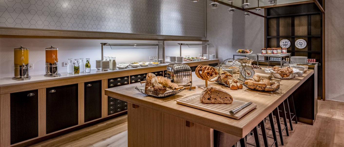 Ein reichhaltiges Frühstücksbuffet mit Brot, Gebäck, Saftspendern und Geschirr in einem modernen, hellen Raum., © Stuttgart Marriott Hotel Sindelfingen