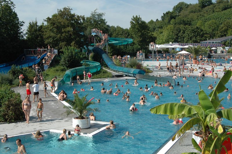 Ein belebtes Freibad mit zahlreichen Menschen im Wasser und auf den Rutschen. Umgeben von Bäumen und Pflanzen, herrscht eine sommerliche Atmosphäre., © Freibad Oberstenfeld Ein belebtes Freibad mit zahlreichen Menschen im Wasser und auf den Rutschen. Umgeben von Bäumen und Pflanzen, herrscht eine sommerliche Atmosphäre., © Freibad Oberstenfeld