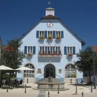 Blaues Gebäude mit Uhr und Blumenkästen, davor ein Brunnen und Café mit Sonnenschirmen, bei sonnigem Wetter., © http://www.rutesheim.de/servlet/PB/menu/1110073/index.html Blaues Gebäude mit Uhr und Blumenkästen, davor ein Brunnen und Café mit Sonnenschirmen, bei sonnigem Wetter., © http://www.rutesheim.de/servlet/PB/menu/1110073/index.html