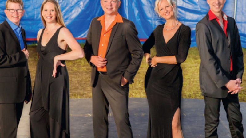 Fünf Personen in eleganter Abendkleidung posieren lächelnd vor einem blauen Hintergrund. Sie tragen Anzüge und Kleider., © Theaterwerkstatt Schwäbisch Gmünd e.V.