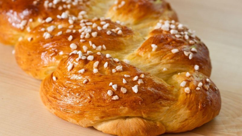 Ein goldbrauner Hefezopf mit Hagelzucker bestreut liegt auf einem Holztisch., © ©Harald Biebel - adobe.stock.com Ein goldbrauner Hefezopf mit Hagelzucker bestreut liegt auf einem Holztisch., © ©Harald Biebel - adobe.stock.com