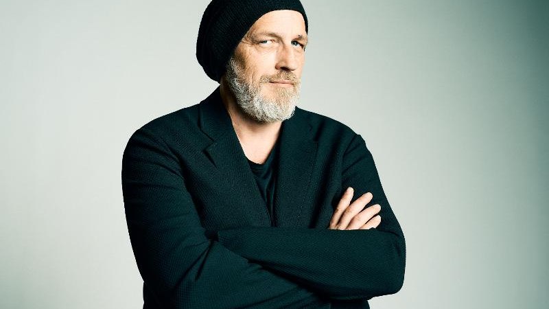 Mann mit Bart und M&uuml;tze, in schwarzer Kleidung, verschr&auml;nkt die Arme vor neutralem Hintergrund., &copy; Roth & Friends