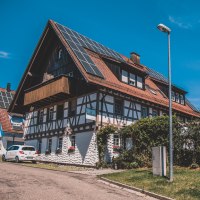 Fachwerkhaus mit Solarpanelen auf dem Dach, umgeben von Bäumen und einem Auto. Klare blaue Himmel und eine Straßenlaterne im Vordergrund., © Stadt Welzheim Fachwerkhaus mit Solarpanelen auf dem Dach, umgeben von Bäumen und einem Auto. Klare blaue Himmel und eine Straßenlaterne im Vordergrund., © Stadt Welzheim