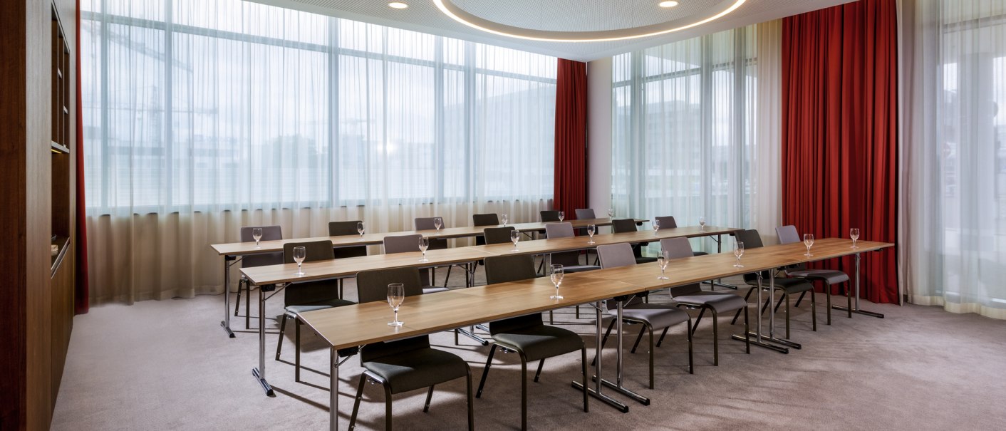 Moderner Tagungsraum mit langen Tischen, Stühlen und Gläsern. Große Fenster mit weißen und roten Vorhängen, runder Deckenleuchter., © Mövenpick Hotel Stuttgart Messe & Congress Moderner Tagungsraum mit langen Tischen, Stühlen und Gläsern. Große Fenster mit weißen und roten Vorhängen, runder Deckenleuchter., © Mövenpick Hotel Stuttgart Messe & Congress