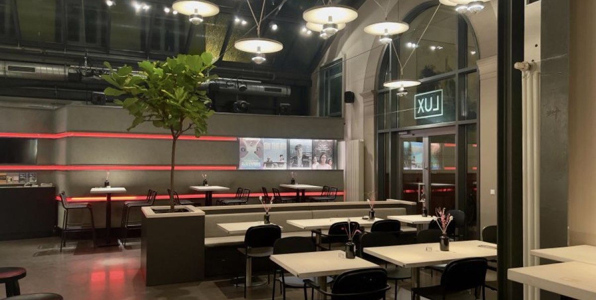 Modernes Café mit stilvoller Beleuchtung, minimalistischen Möbeln und einem Baum in der Mitte. Der Raum wirkt einladend und elegant., © Kinogastronomie LUX Modernes Café mit stilvoller Beleuchtung, minimalistischen Möbeln und einem Baum in der Mitte. Der Raum wirkt einladend und elegant., © Kinogastronomie LUX