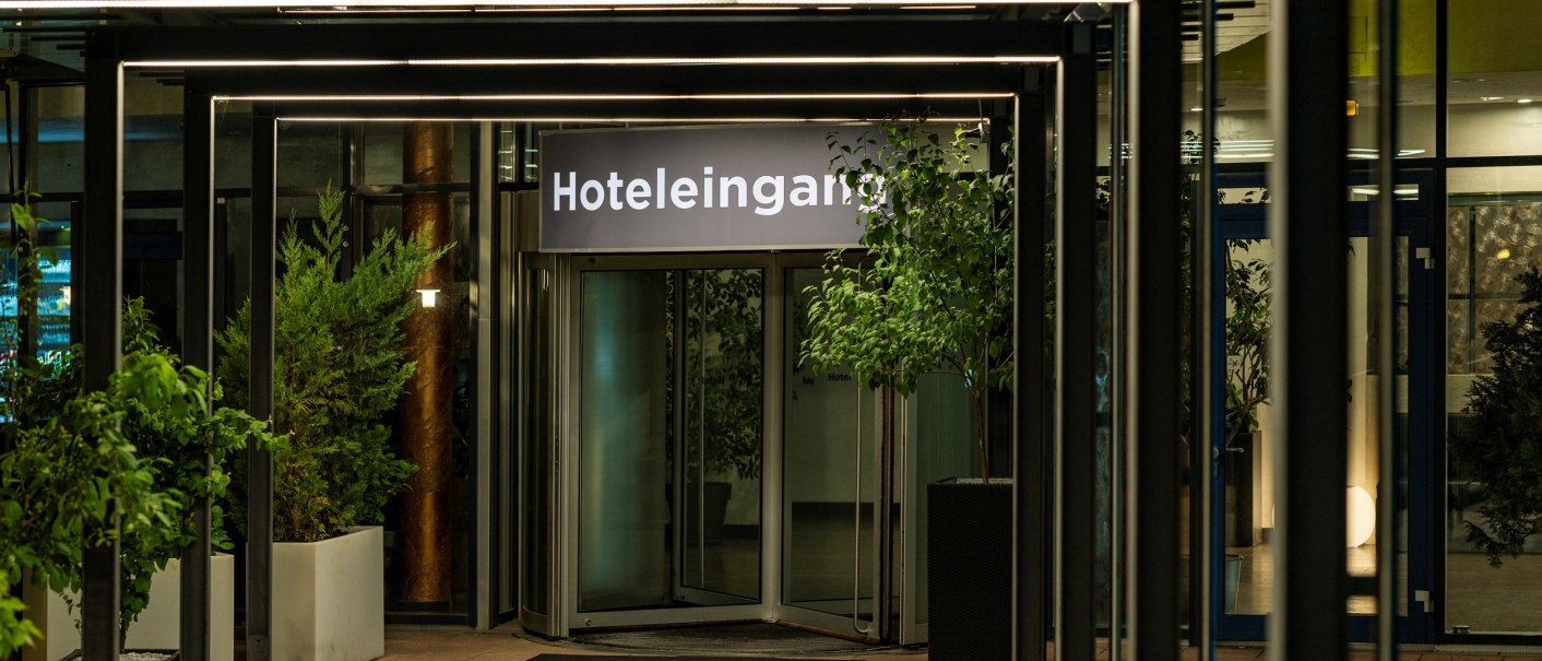 Beleuchteter Hoteleingang mit Pflanzen in Töpfen und einem Schild mit der Aufschrift 'Hoteleingang'., © Plaza Residence Stuttgart-Ditzingen Beleuchteter Hoteleingang mit Pflanzen in Töpfen und einem Schild mit der Aufschrift 'Hoteleingang'., © Plaza Residence Stuttgart-Ditzingen