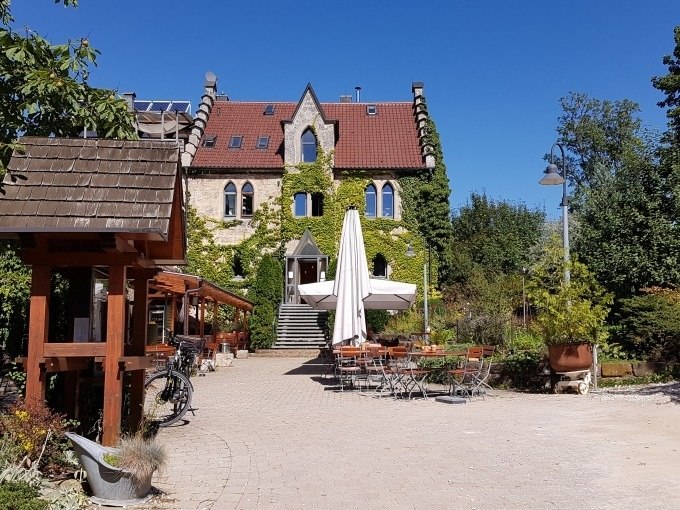Historisches Geb&auml;ude mit rotem Dach und Efeu bewachsen. Davor ein Garten mit Sitzbereich und Sonnenschirm. Klarer blauer Himmel im Hintergrund., &copy; SwabianTravel