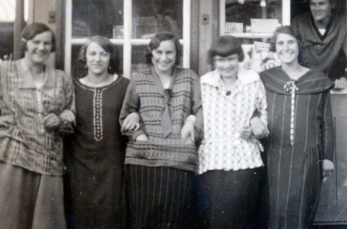 Fünf Frauen in Vintage-Kleidung stehen Arm in Arm vor einem Geschäft. Eine sechste Person schaut aus dem Fenster. Die Szene wirkt freundlich und nostalgisch., © Eigenbetrieb Tourismus und Citymanagement Schorndorf