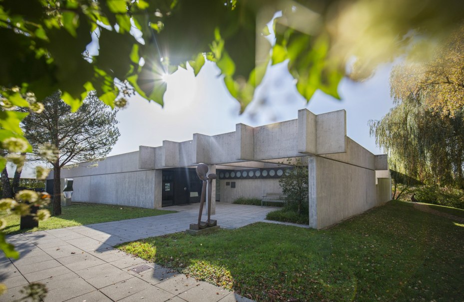 Modernes Betongebäude mit Skulptur im Vordergrund, umgeben von Bäumen und Sonnenschein. Die Architektur ist kantig und minimalistisch., © © Copyright by MICHAEL STEINERT FOTOGRAFIE Modernes Betongebäude mit Skulptur im Vordergrund, umgeben von Bäumen und Sonnenschein. Die Architektur ist kantig und minimalistisch., © © Copyright by MICHAEL STEINERT FOTOGRAFIE