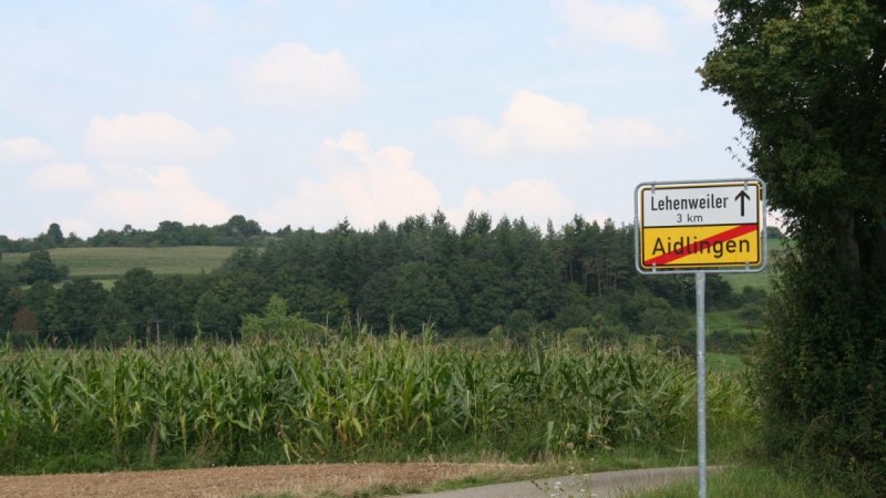 Stra&szlig;enschild zeigt das Ende von Aidlingen und Richtung nach Lehenweiler. Umgebung mit Feldern und B&auml;umen, blauer Himmel im Hintergrund., &copy; Natur.Nah. Sch&ouml;nbuch & Heckeng&auml;u