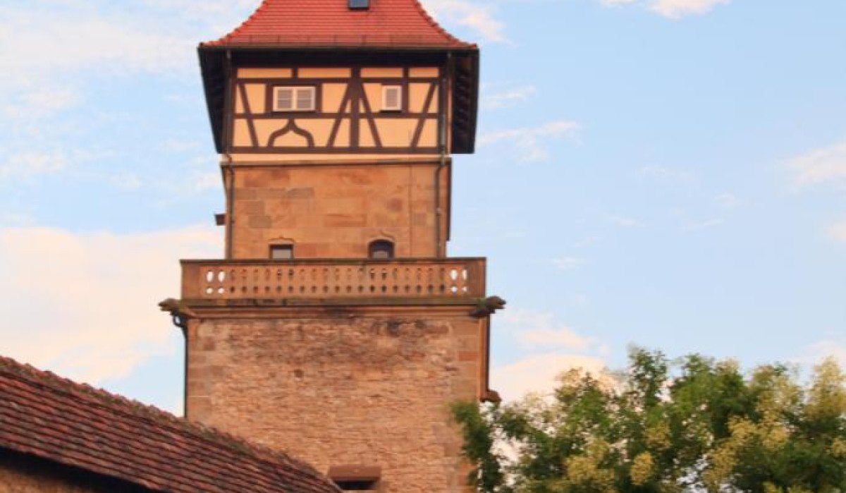 Ein historischer Wachturm mit Fachwerk und rotem Dach, umgeben von Bäumen und einer Steinmauer, vor einem blauen Himmel mit Wolken., © Waiblingen - Stuttgart-Marketing GmbH Ein historischer Wachturm mit Fachwerk und rotem Dach, umgeben von Bäumen und einer Steinmauer, vor einem blauen Himmel mit Wolken., © Waiblingen - Stuttgart-Marketing GmbH