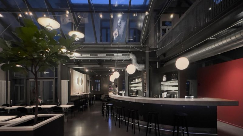 Modernes Caf&eacute; mit Glasdach, stilvoller Beleuchtung und eleganter Bar. Dunkle M&ouml;bel und Pflanzen schaffen eine gem&uuml;tliche Atmosph&auml;re., &copy; Kinogastronomie LUX