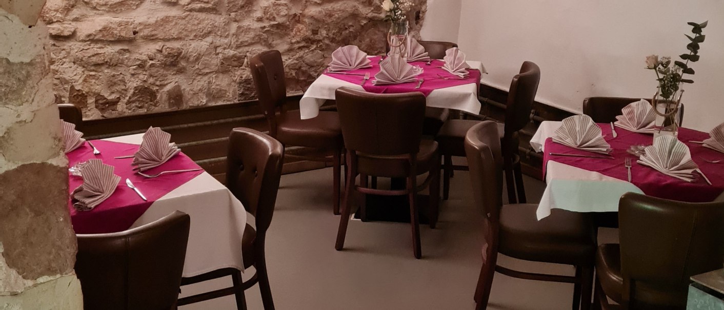 Ein gem&uuml;tlicher Kellerraum mit Steinw&auml;nden und gew&ouml;lbter Decke. Die Tische sind mit wei&szlig;en Tischdecken und roten Servietten dekoriert., &copy; DaInes