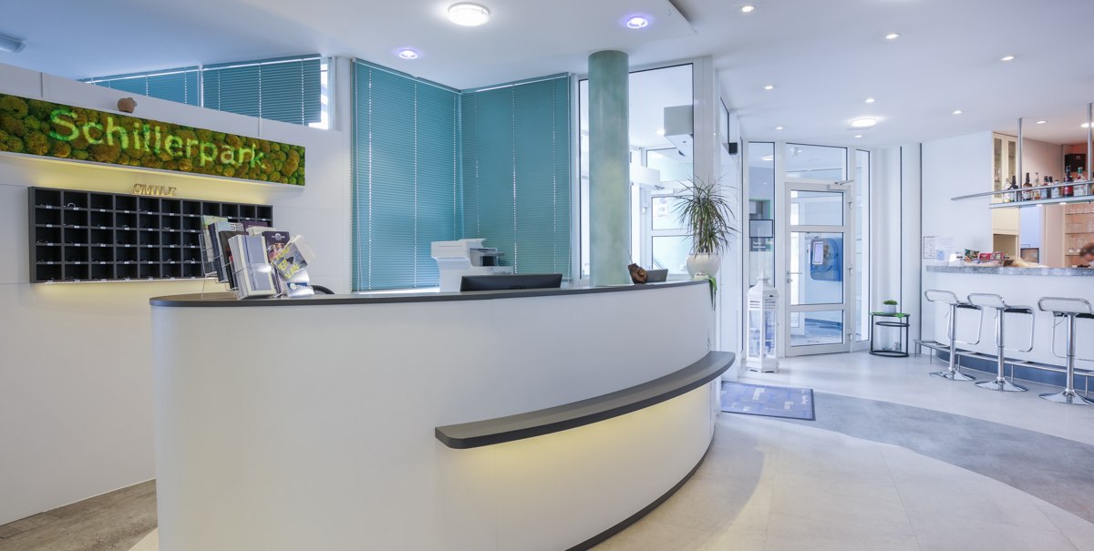 Moderne Rezeption mit geschwungenem Tresen, grüner Dekoration und Barbereich im Hintergrund. Helle, einladende Atmosphäre., © TOMAS Moderne Rezeption mit geschwungenem Tresen, grüner Dekoration und Barbereich im Hintergrund. Helle, einladende Atmosphäre., © TOMAS