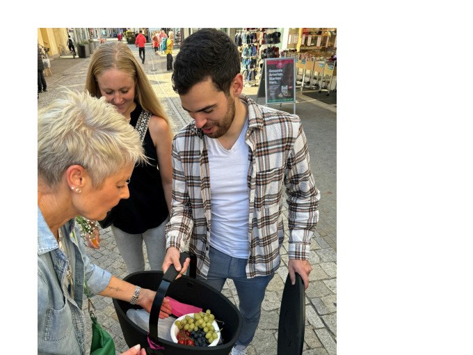 Drei Personen stehen in einer Fu&szlig;g&auml;ngerzone und betrachten einen Picknickkorb mit Trauben und Beeren., &copy; Eigenbetrieb Tourismus und Citymanagement Schorndorf