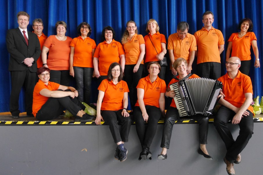 Der Akkordeon-Club Bonlanden posiert in orangen T-Shirts vor einem blauen Vorhang. Eine Person h&auml;lt ein Akkordeon., &copy; Akkordeon-Club Bonlanden