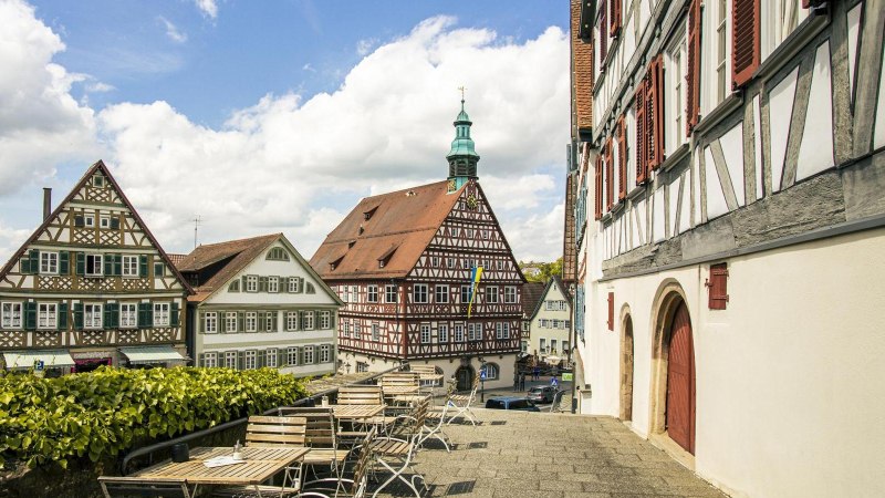 Blick auf historische Fachwerkhäuser in Backnang. Im Vordergrund leere Sitzplätze, im Hintergrund ein blauer Himmel mit Wolken., © SMG, Sarah Schmid Blick auf historische Fachwerkhäuser in Backnang. Im Vordergrund leere Sitzplätze, im Hintergrund ein blauer Himmel mit Wolken., © SMG, Sarah Schmid
