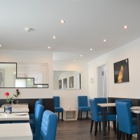 Moderner Frühstücksraum mit blauen Stühlen, weißen Tischen und dekorativen Bildern an den Wänden. Dezente Beleuchtung und stilvolle Dekoration., © Hotel BaWü Moderner Frühstücksraum mit blauen Stühlen, weißen Tischen und dekorativen Bildern an den Wänden. Dezente Beleuchtung und stilvolle Dekoration., © Hotel BaWü