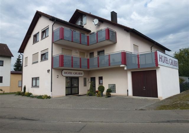 Das Hotel Gruber in Schorndorf zeigt eine helle Fassade mit roten Balkonen und einem Eingangsschild. Es liegt an einer ruhigen Straße., © Hotel Gruber Das Hotel Gruber in Schorndorf zeigt eine helle Fassade mit roten Balkonen und einem Eingangsschild. Es liegt an einer ruhigen Straße., © Hotel Gruber