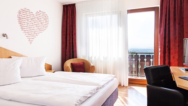 Helles Doppelzimmer mit großem Bett, rotem Vorhang, Sessel, Schreibtisch mit Fernseher und Balkon mit Aussicht., © Hotel Restaurant Kaiser