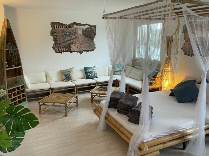 Ein gemütlicher Raum mit Bambusmöbeln, Himmelbett, Sofas und Stranddeko. Handtücher liegen auf dem Bett bereit., © Cool-Tours StattReisen Ein gemütlicher Raum mit Bambusmöbeln, Himmelbett, Sofas und Stranddeko. Handtücher liegen auf dem Bett bereit., © Cool-Tours StattReisen
