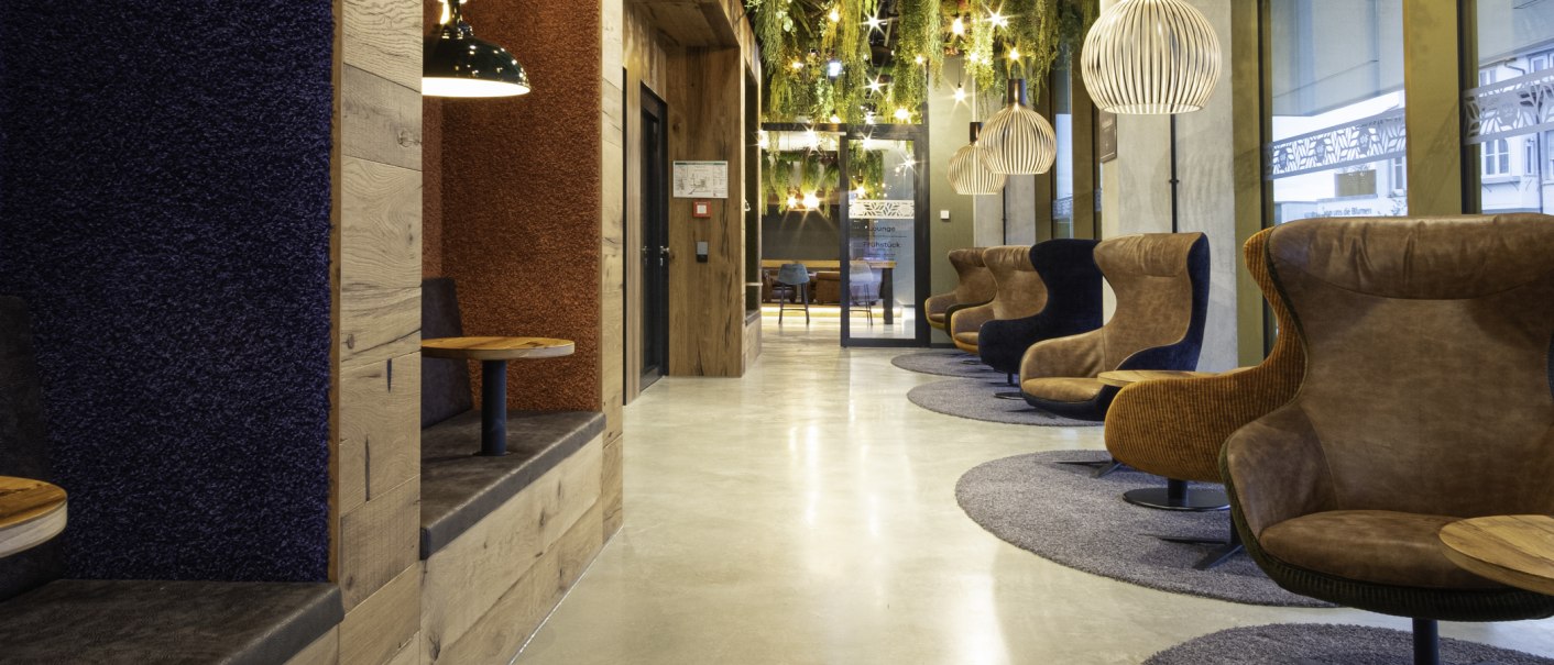 Moderne Hotellobby mit gemütlichen Sesseln, Holzelementen und hängenden Pflanzen. Warme Beleuchtung und stilvolle Einrichtung schaffen eine einladende Atmosphäre., © 13 6 Design GmbH (Judenhof 10, 89073 Ulm)