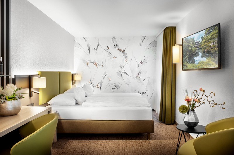 Modernes Hotelzimmer mit Doppelbett, stilvoller Wandgestaltung, Schreibtisch und TV. Elegante Beleuchtung und Dekoration schaffen eine einladende Atmosphäre., © TOMAS