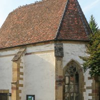 Historische Kirche mit rotem Ziegeldach, gotischem Fenster und Tauben auf dem Dach. Ein Baum und ein Schild sind ebenfalls sichtbar., © Alex Becher Historische Kirche mit rotem Ziegeldach, gotischem Fenster und Tauben auf dem Dach. Ein Baum und ein Schild sind ebenfalls sichtbar., © Alex Becher