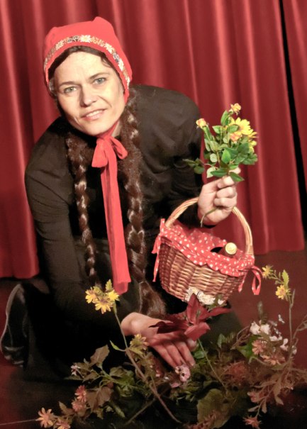 Eine Person im Rotkäppchen-Kostüm hält einen Korb und Blumen vor einem roten Vorhang., © Galli Theater Backnang