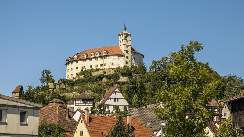 Schloss Kaltenstein thront auf einem Hügel, umgeben von Bäumen, mit traditionellen Häusern im Vordergrund und klarem Himmel im Hintergrund., © Stuttgart-Marketing GmbH, Sarah Schmid