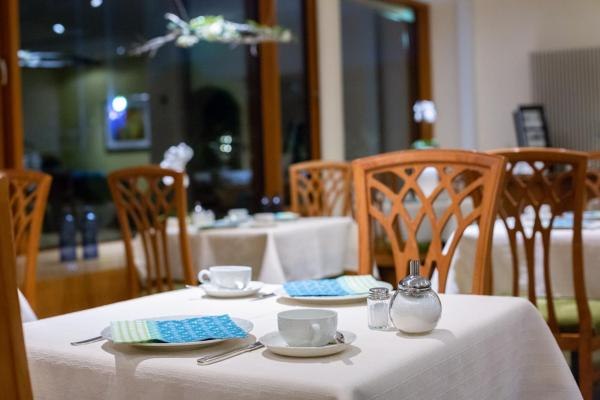 Ein eleganter Frühstücksraum mit gedeckten Tischen, Tassen, Besteck und Servietten. Holzmöbel und große Fenster sorgen für eine einladende Atmosphäre., © Kronen Hotel GmbH