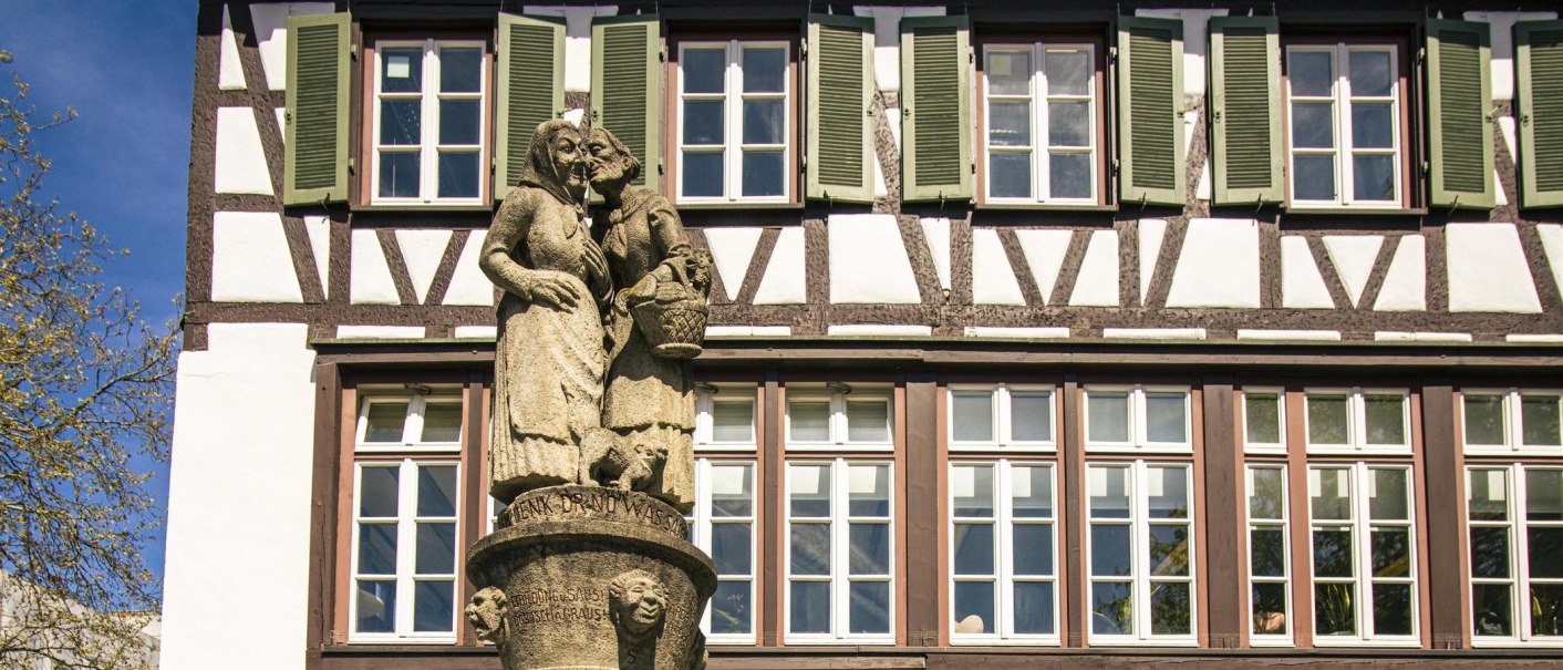 Der Schw&auml;tzweiberbrunnen in Sindelfingen zeigt zwei Frauenfiguren aus Stein, die sich unterhalten. Im Hintergrund ist ein Fachwerkhaus zu sehen., &copy; SMG, Sarah Schmid