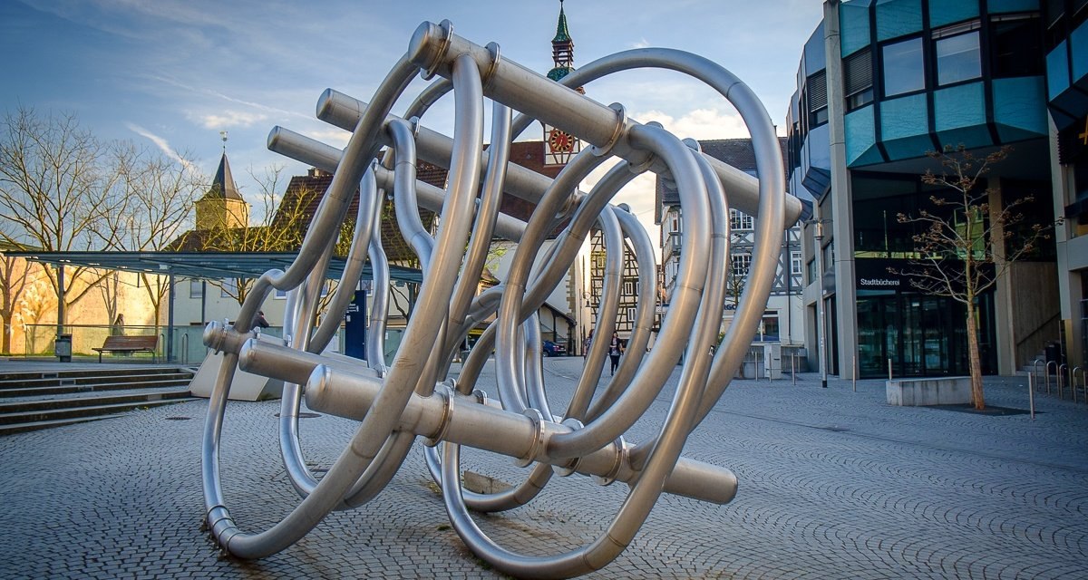 Metallskulptur aus verschlungenen Rohren auf einem Platz, umgeben von modernen und historischen Gebäuden., © Remstal Tourismus e.V. Metallskulptur aus verschlungenen Rohren auf einem Platz, umgeben von modernen und historischen Gebäuden., © Remstal Tourismus e.V.