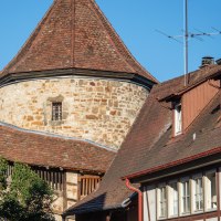 Der Blockturm in Nürtingen ist zwischen zwei Häusern sichtbar. Der Turm hat ein rundes, steinernes Mauerwerk und ein spitzes, rotes Ziegeldach., © SMG, Achim Mende