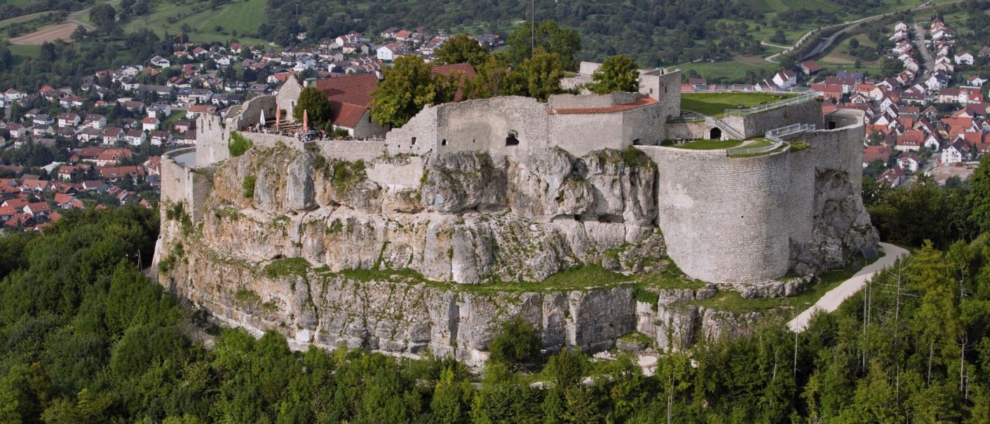 Die Ruine Hohenneuffen thront auf einem Hügel, umgeben von grüner Landschaft und einer Siedlung im Hintergrund., © Stuttgart-Marketing GmbH